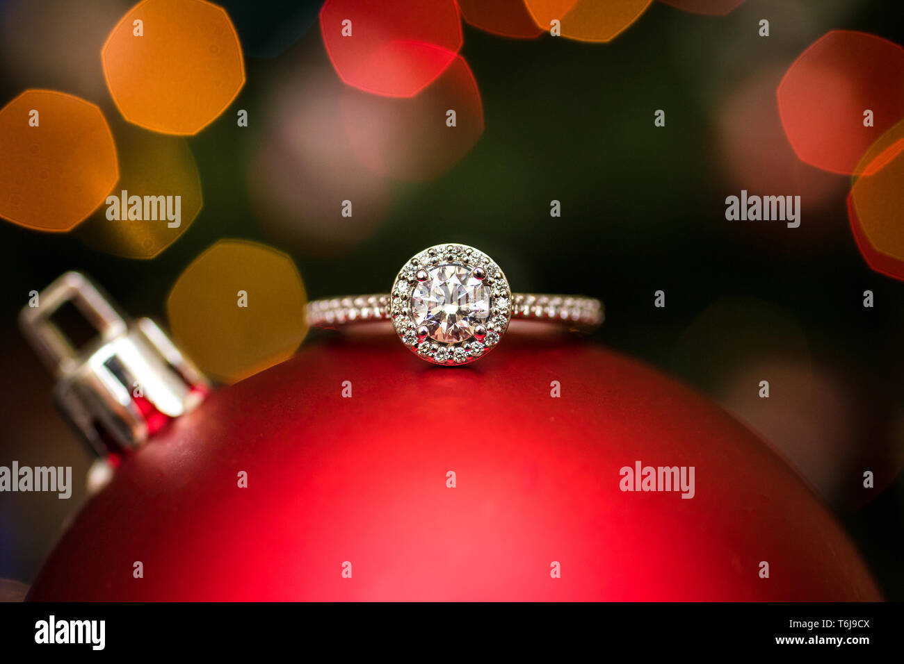 Engagement ring on a Christmas ornament with lights in the background