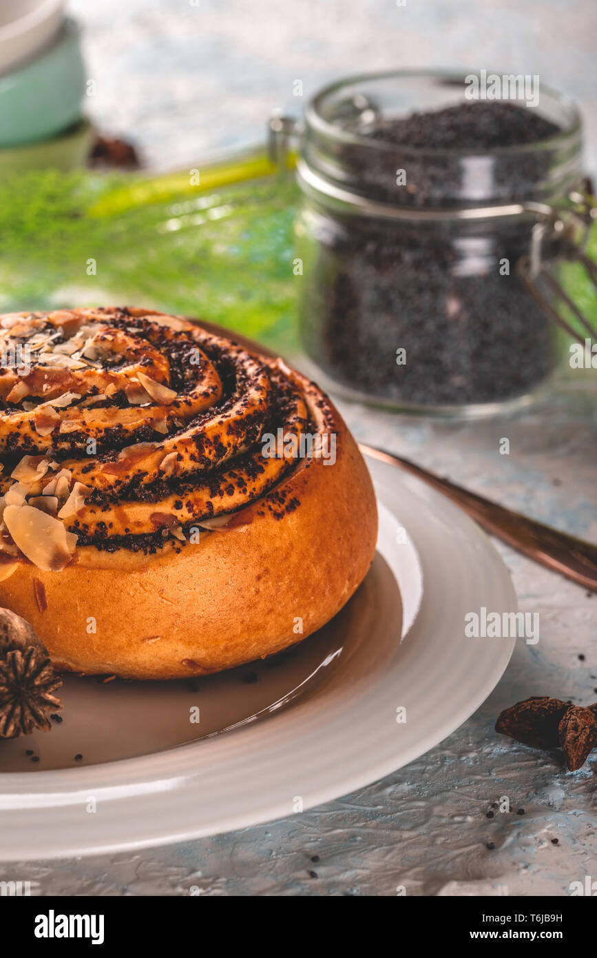 Vertical photo of glass jar full of black poppy seeds with sealed cover. Jar is on wooden board with nice white and blue texture. Sweet bun with poppy Stock Photo