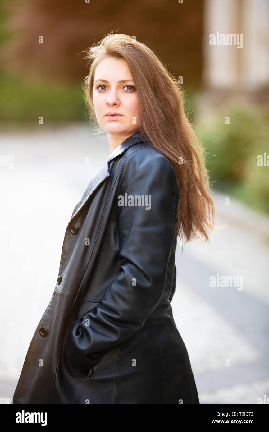 portrait of young brunette woman in leather jacket standing outside ...
