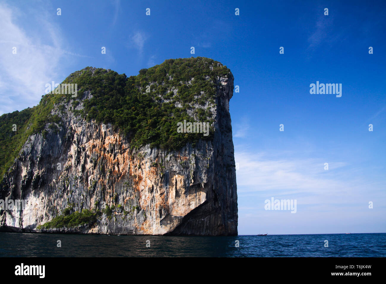 Isolated steep rough cliff in the ocean rising into blue sky of tropical island Ko Phi Phi, Thailand Stock Photo