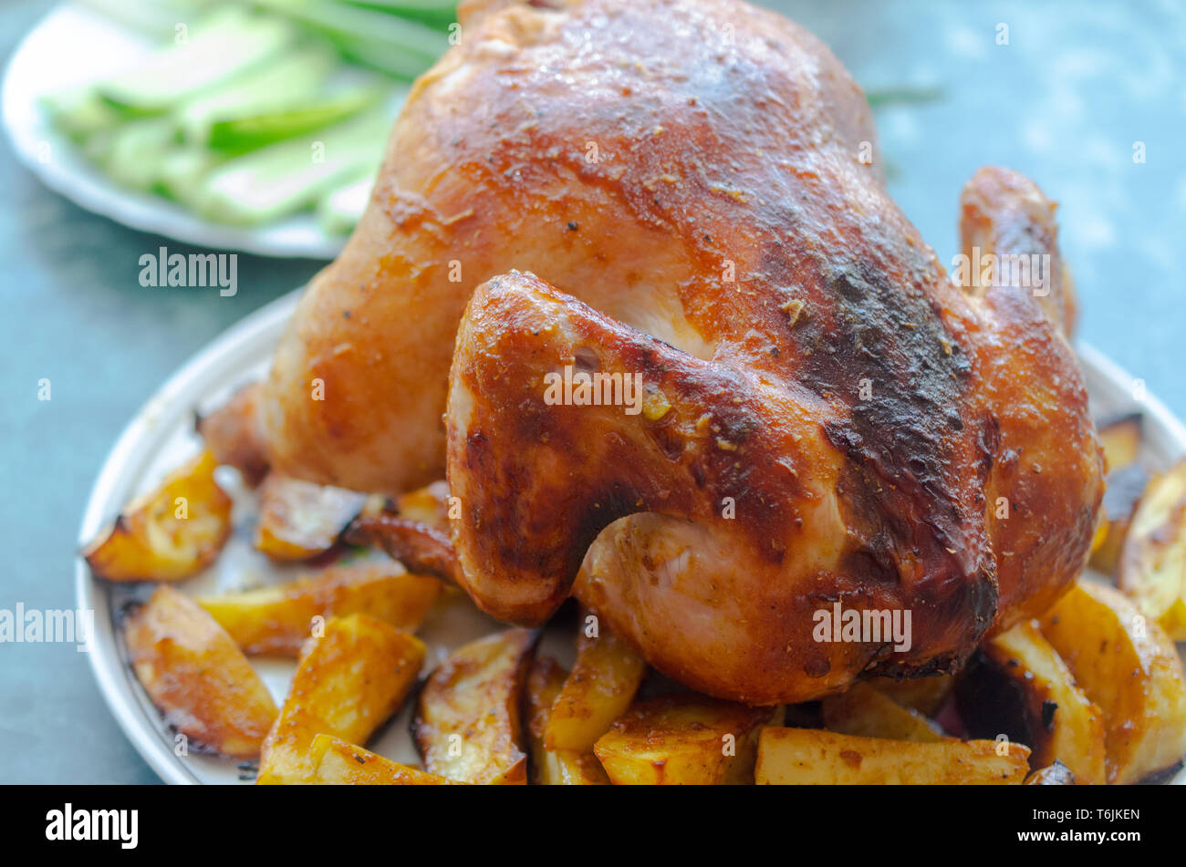 Chicken from the oven on a white plate with greens and potatoes with a golden crust Stock Photo
