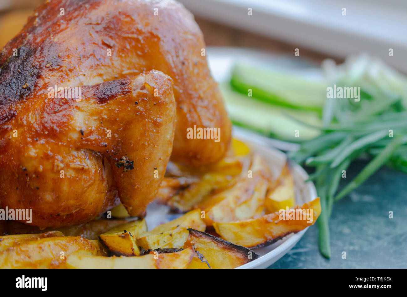 Chicken from the oven on a white plate with greens and potatoes with a golden crust Stock Photo
