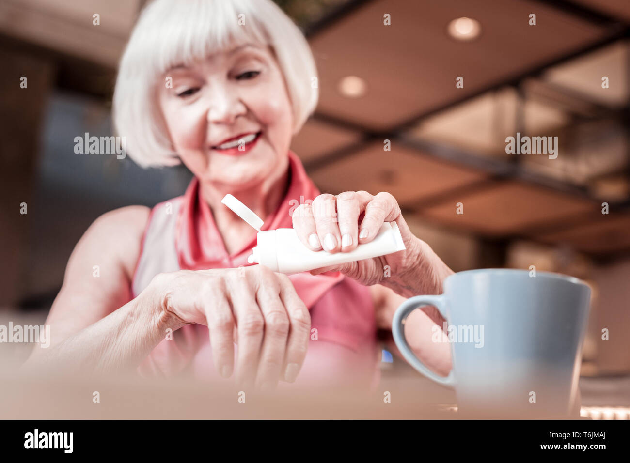 Beaming blonde old woman carrying tube with hand cream Stock Photo