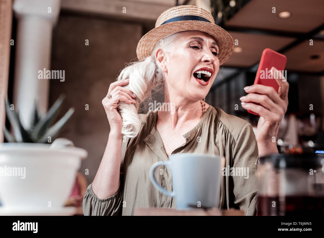Coquettish loud senior lady in straw hat checking her smartphone Stock Photo