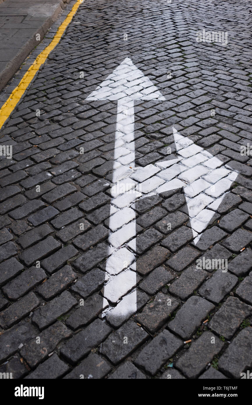 cobbled street with white arrow painted on the surface, straight ahead or right turn, concept. Stock Photo