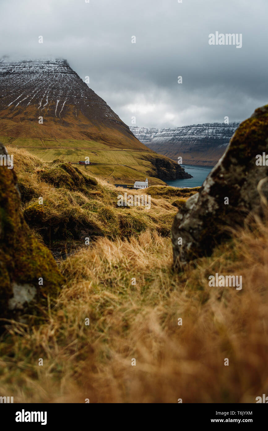 View from Kap Enniberg towards the small village Viðareiði, Viðareiði kirkja, its fjord and snow-covered mountains (Faroe Islands, Denmark, Europe) Stock Photo