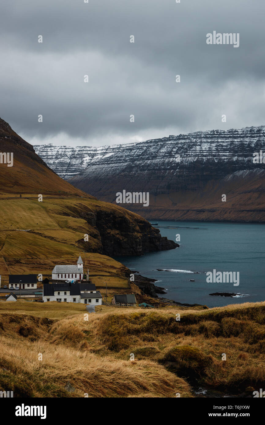 View from Kap Enniberg towards the small village Viðareiði, Viðareiði kirkja, its fjord and snow-covered mountains (Faroe Islands, Denmark, Europe) Stock Photo