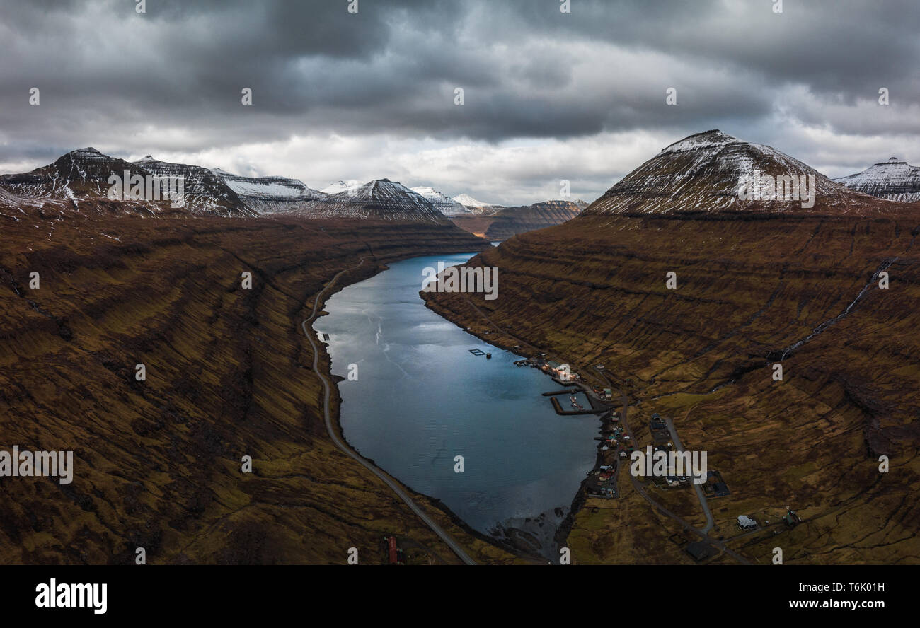 Aerial panoramic view of the fjord of Funningsfjørður with dramatic cloudy sky and snow-covered mountains (Faroe Islands, Denmark, Europe) Stock Photo