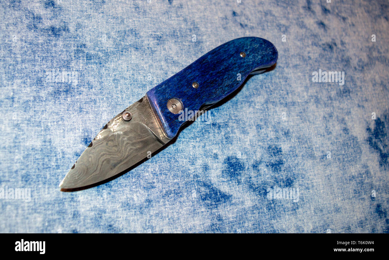 Damascus pocket knife with blue camel bone handle displayed on blue and white fabric. Stock Photo