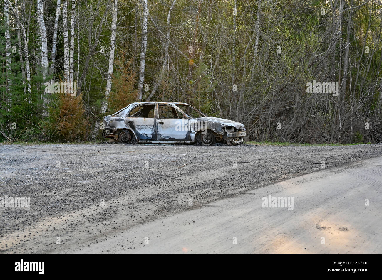 a burnt down car at a gravel road Stock Photo