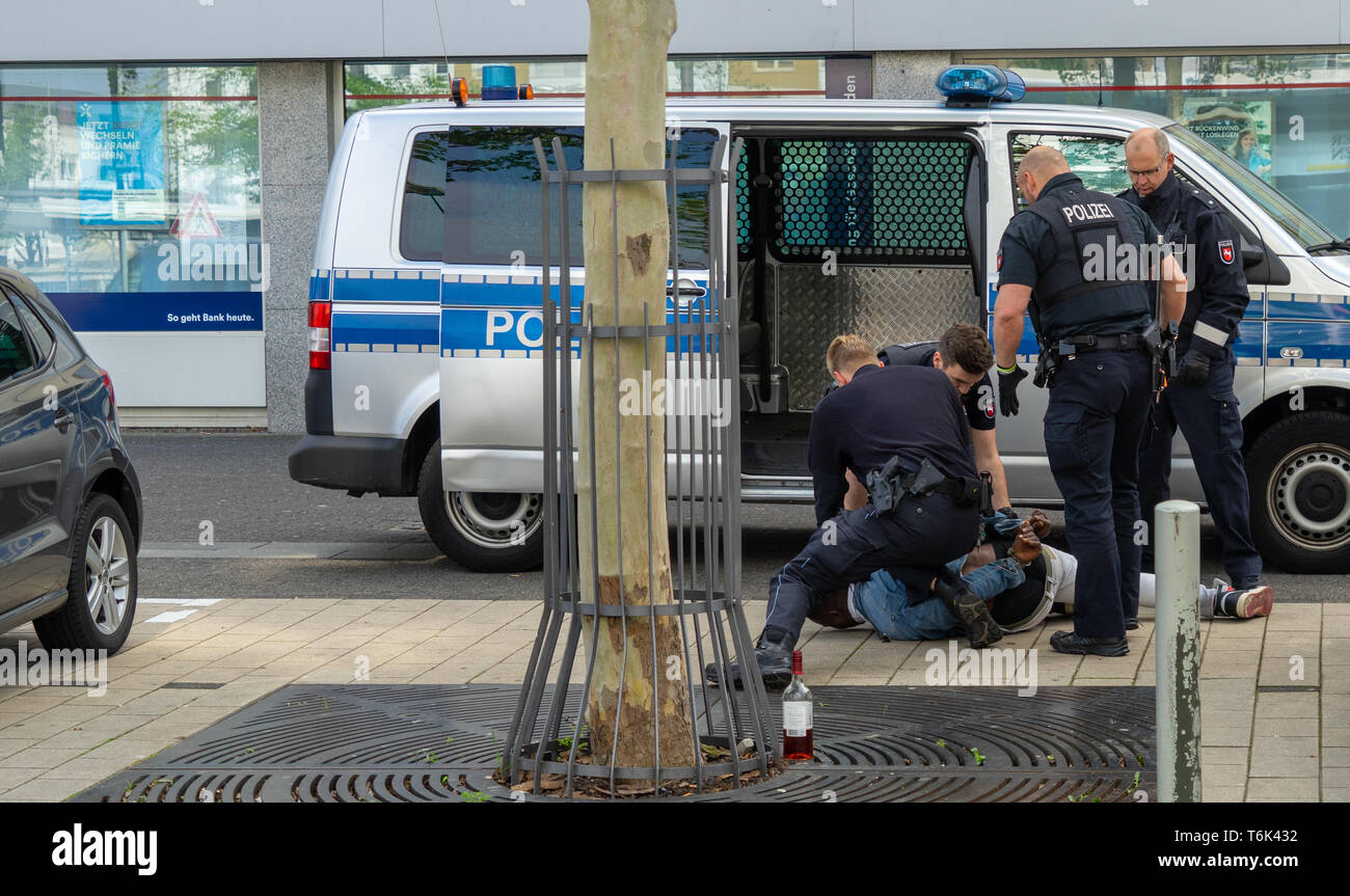 Wolfsburg, Germany, May 1, 2019: A dark-skinned man is handcuffed by German police officers in black uniforms and held at the bottom of the sidewalk,  Stock Photo