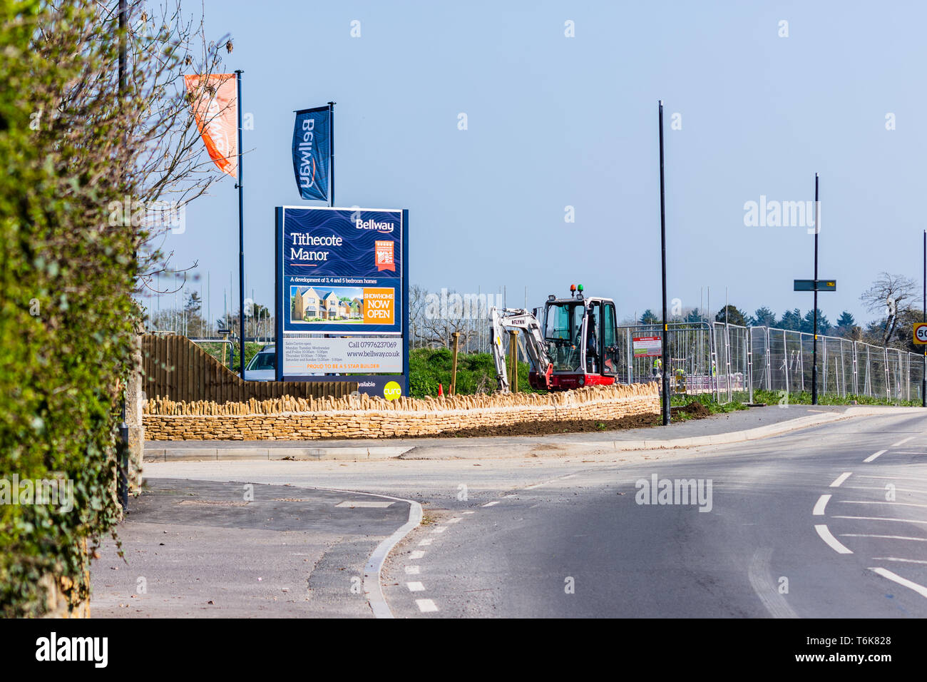 A sign flags of a new housing development Tithecote Manor by Bellway in Bradford on Avon Wiltshire with fencing a small digger next to the sign. Stock Photo