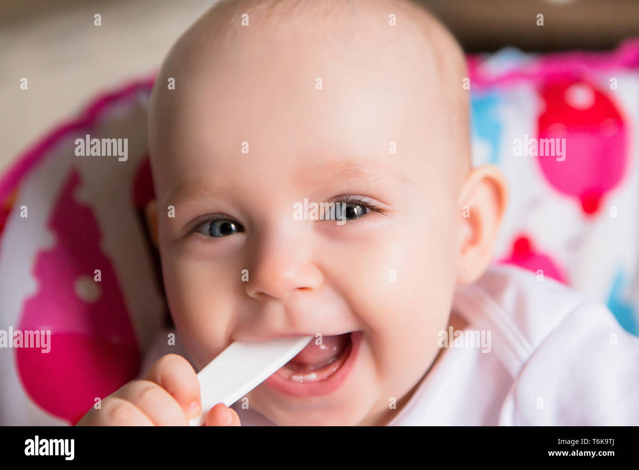 Baby in the kitchen in a baby chair holding a spoon and smiling.Sweet baby in high chair