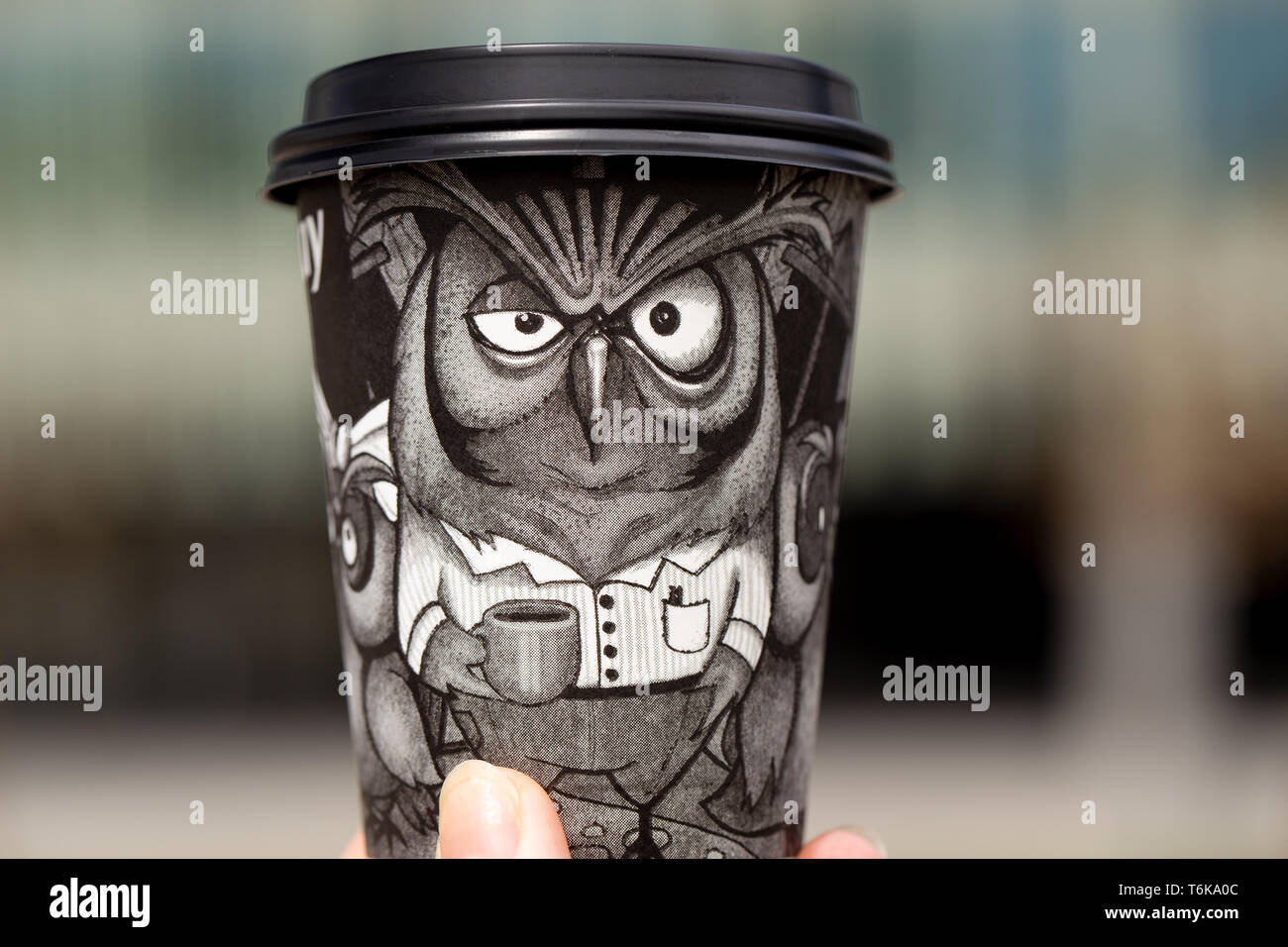 Black paper disposable coffee cup with a drawn owl in hand on a blurred ...