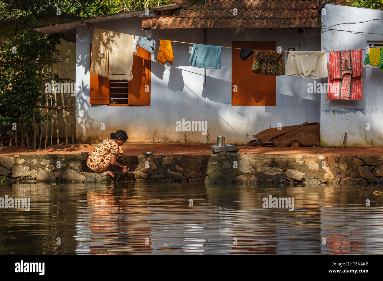 Woman in yellow print dress working at edge of river in front of her