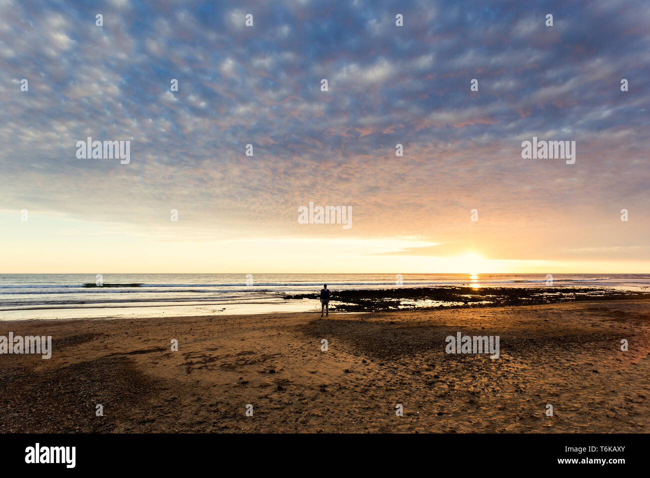 A man is watching a beautiful sunset over the mediterranean sea while standing near the shore, Chipiona, Cádiz, Spain Stock Photo
