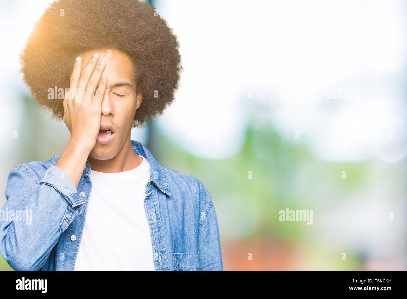 Young african american man with afro hair Yawning tired covering half