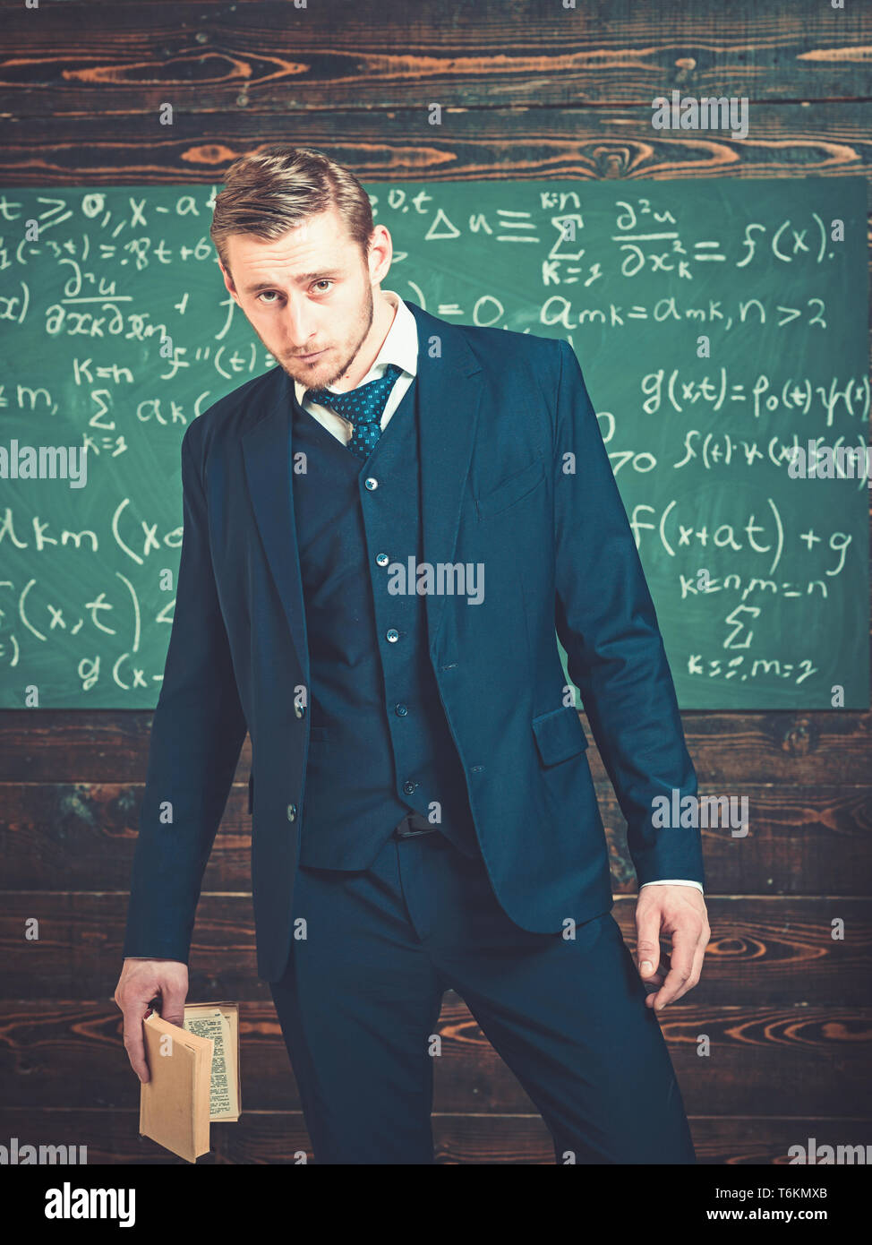 Young student standing with book in his hand. Gentleman in suit and tie  standing in classroom Stock Photo - Alamy