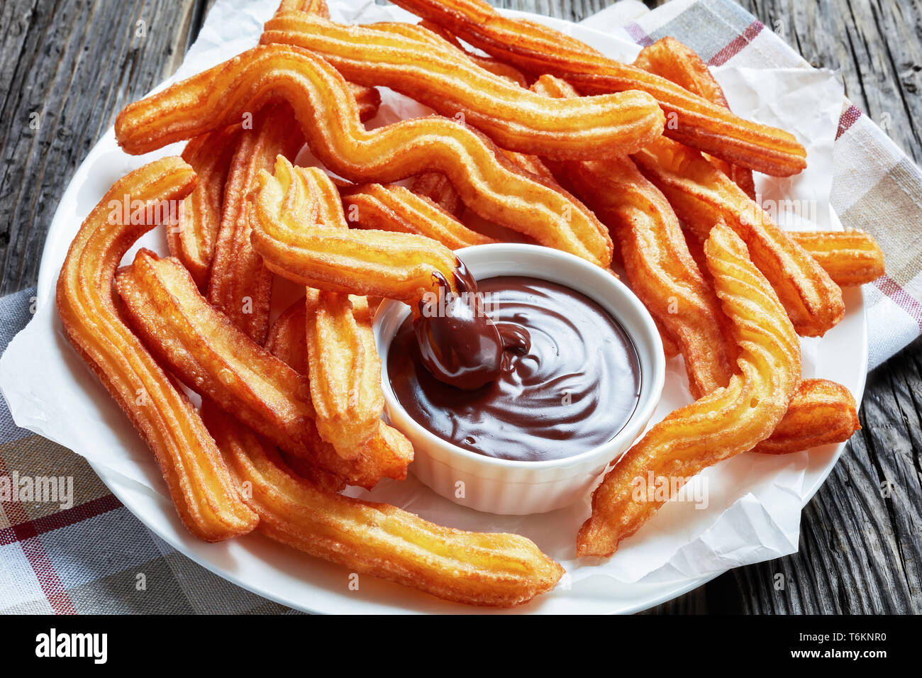 delicious deep fried churros served with chocolate dipping on a white plate on a wooden table with napkin, Traditional spanish and mexican street food Stock Photo