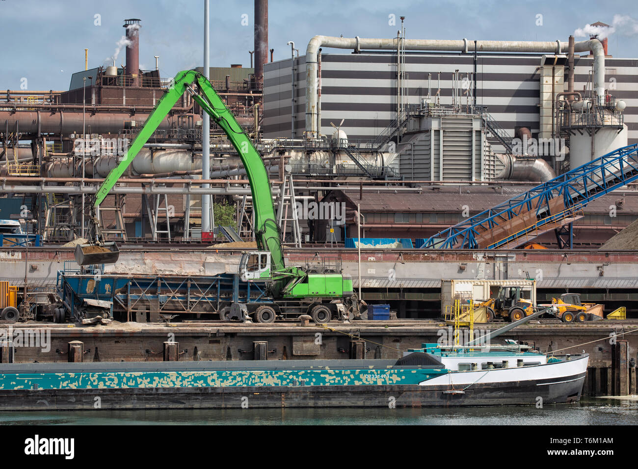 Steel factory in Dutch harbor IJmuiden with crane unloading barge Stock Photo
