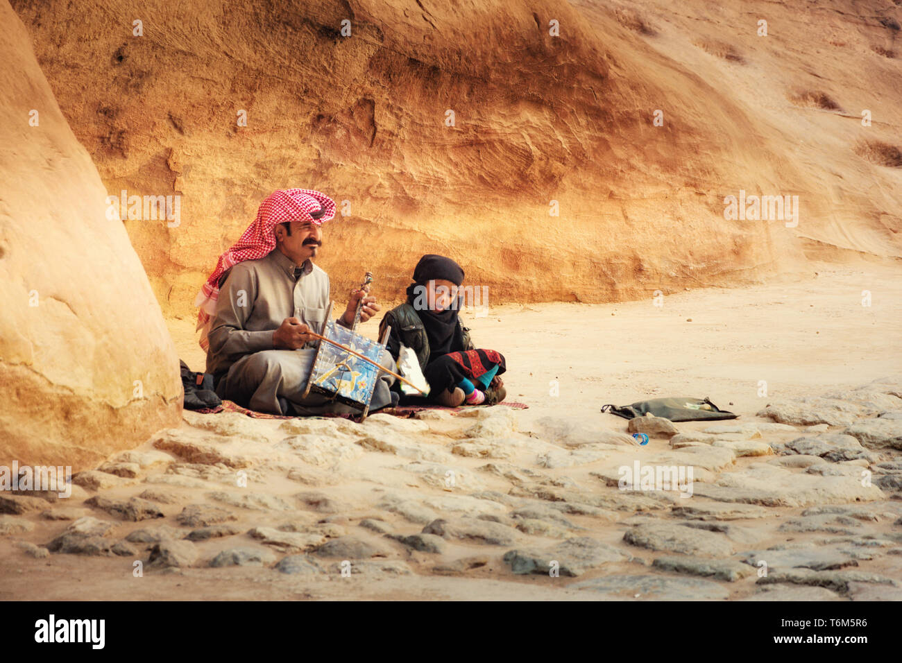 Beduin man playing traditional Bedouin Rababa string musical instruments with his son in ancient city of Petra, Jordan Stock Photo