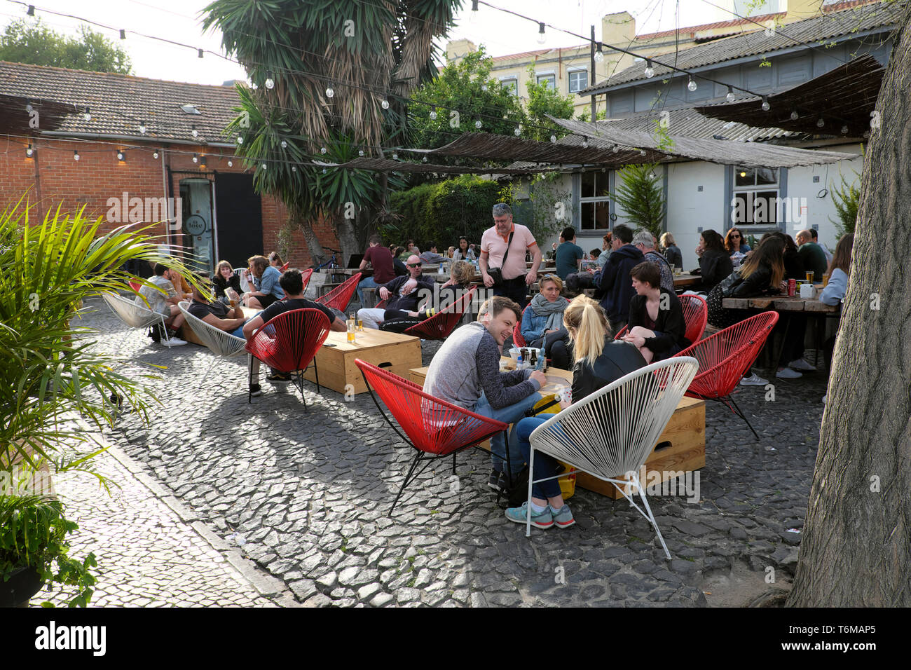 People sitting at tables and in chairs at an outdoor restaurant cafe at the LX Factory in the Alcântara district Lisbon Lisboa Portugal  KATHY DEWITT Stock Photo
