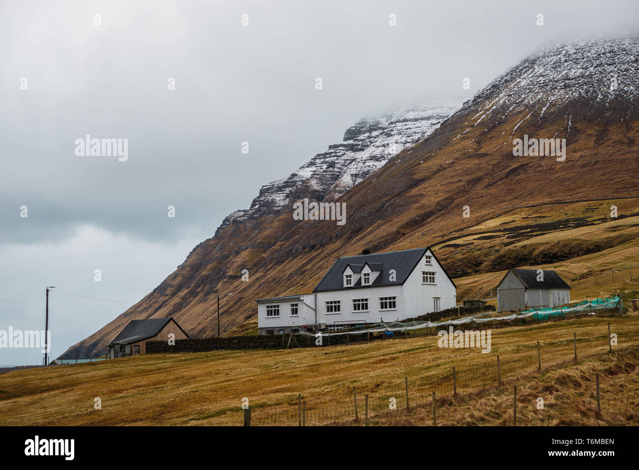 Typical Faroese white wooden house in Viðareiði with fog and snow-covered mountains (Kap Enniberg) in the background (Faroe Islands, Denmark, Europe) Stock Photo