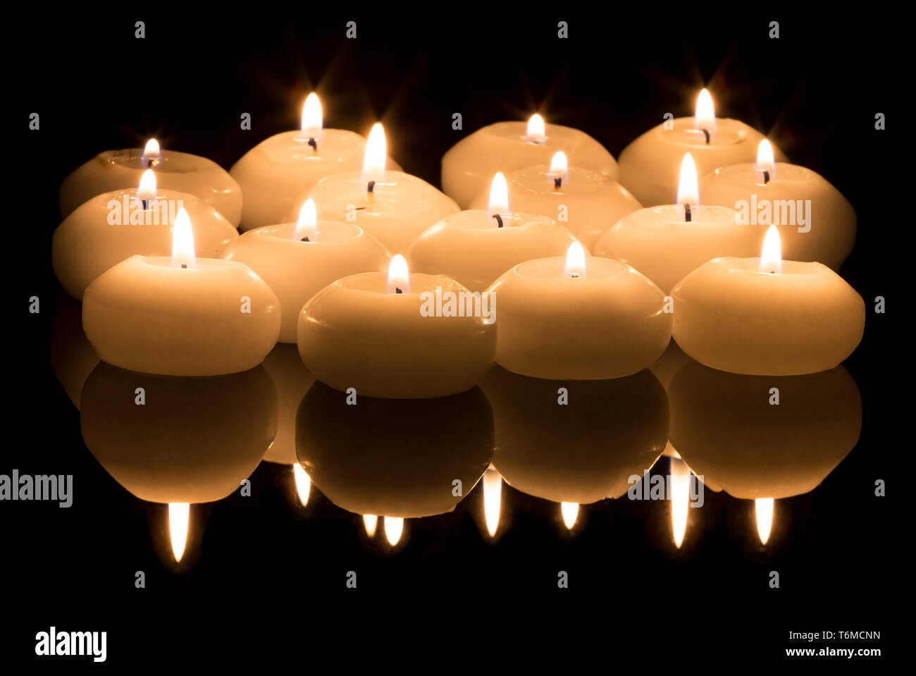 White candles on a black reflecting background Stock Photo