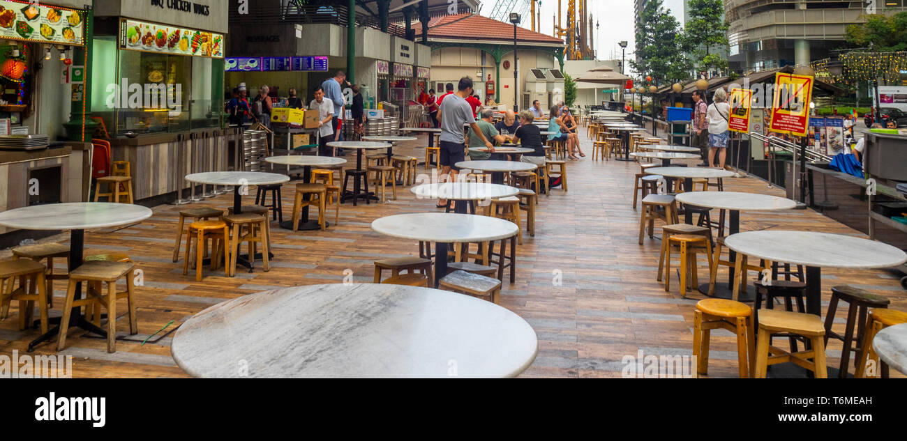 Diners sitting on stools at round tables al fresco outside Lau Pa Sat Hawker Food markets in downtown Singapore. Stock Photo