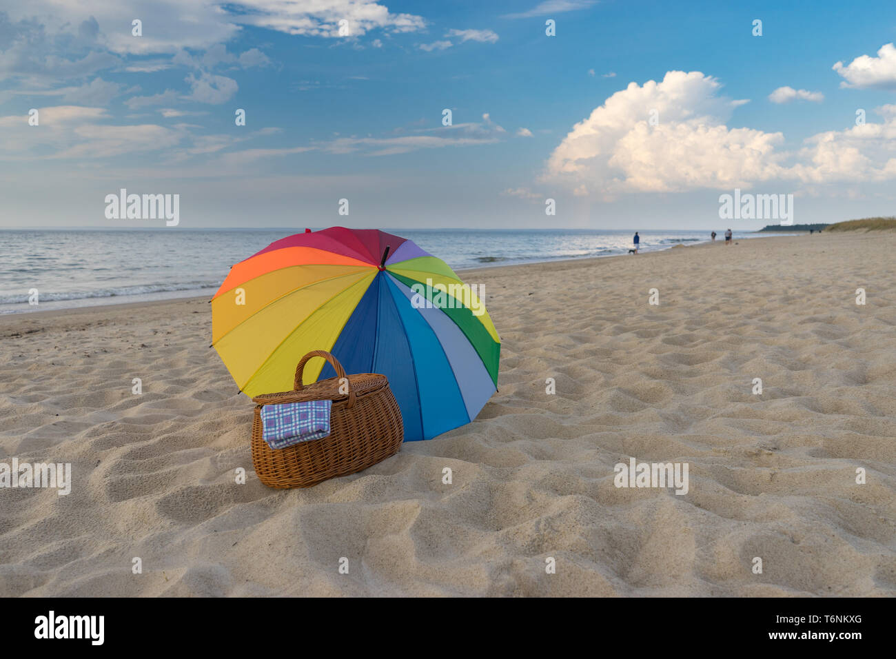 Multicolored umbrella and picnic basket against scenic seacoast, weekend break concept Stock Photo