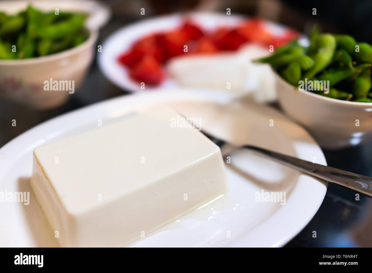 Plate of plain boiled or cold tofu in restaurant or house with vegetable dish snack of boiled edamame and fork Stock Photo