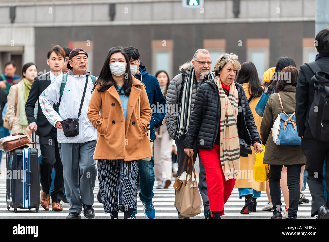 Tokyo, Japan - March 31, 2018: Ginza district with many people local Japanese walking crossing street with woman in mask Stock Photo