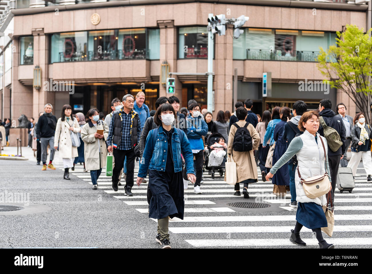 Tokyo, Japan - March 31, 2018: Ginza district with many people Japanese walking crossing street with woman in mask Stock Photo