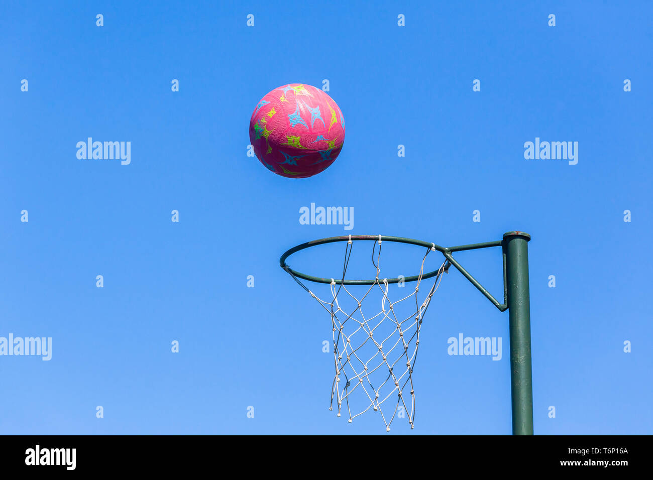 Netball hoop net with red ball in flight against  blue sky . Stock Photo