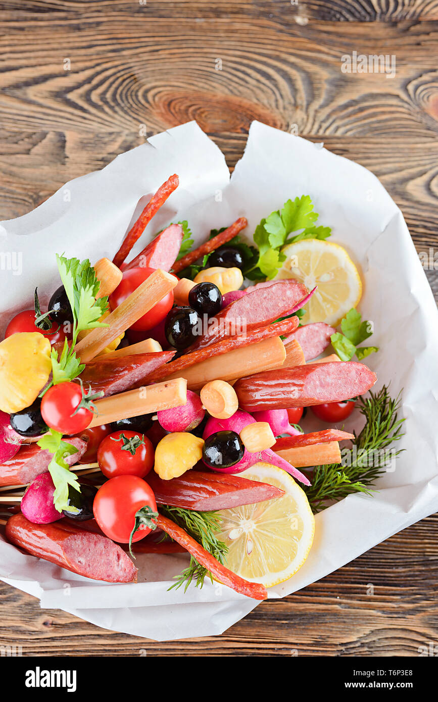 Smoked sausage, cheese, vegetables and greens, collected in a bouquet. Option gift man. On wooden background. Stock Photo