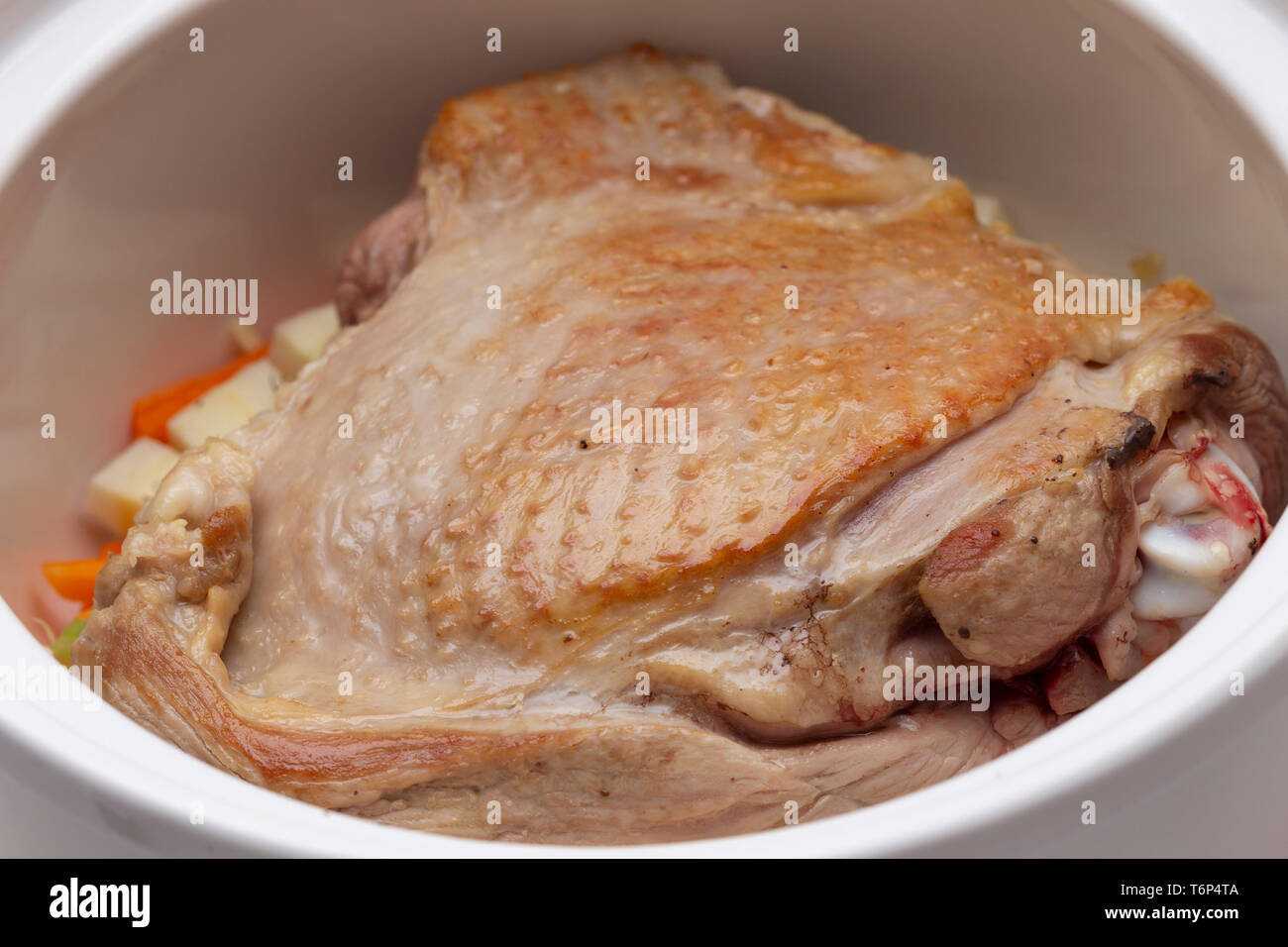 Turkey thigh in a casserole dish with vegertables and provencal herbs, the sking browned ready for braising. Stock Photo