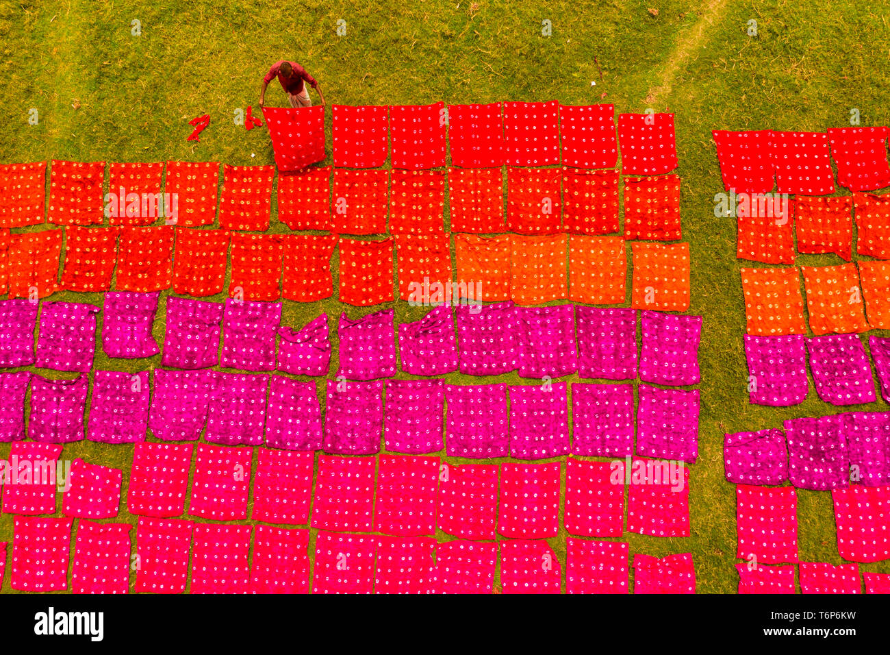 (EDITORS NOTE: Image taken with drone) Workers seen unfolding hundreds of meters of freshly dyed bright red cloth across a field as part of the process of creating traditional Batik.  In this techniques wax is used to create stunning patterns on a huge scale. The wax prevents the dye from penetrating the area it is placed on, allowing workers to create amazingly complex multi-coloured designs. They then soak the cloth in a dying emulsion before rolling the large cotton, silk, or wool cloths in the hot sun to dry. Stock Photo