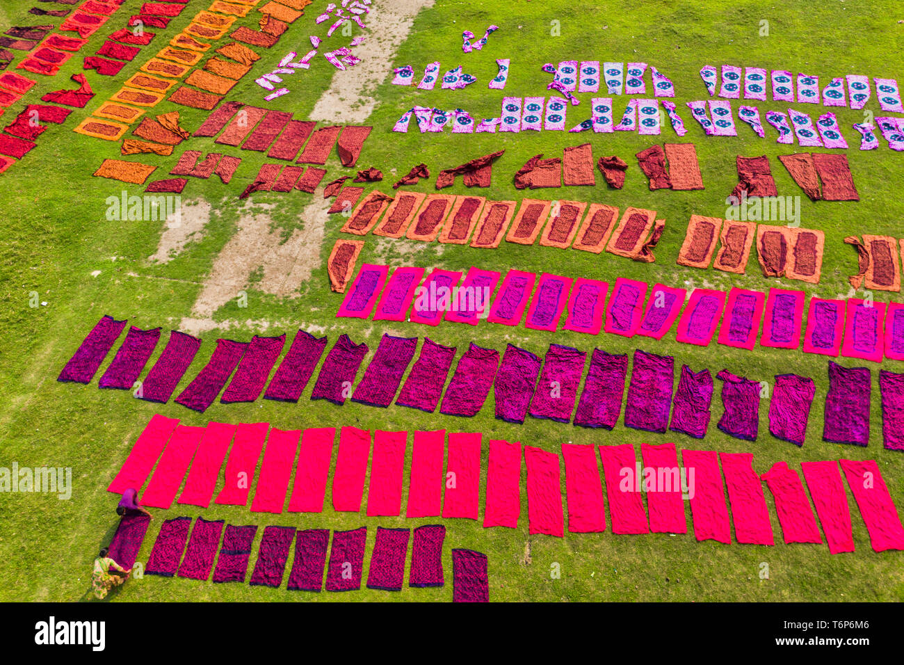 (EDITORS NOTE: Image taken with drone) Workers seen unfolding hundreds of meters of freshly dyed bright red cloth across a field as part of the process of creating traditional Batik.  In this techniques wax is used to create stunning patterns on a huge scale. The wax prevents the dye from penetrating the area it is placed on, allowing workers to create amazingly complex multi-coloured designs. They then soak the cloth in a dying emulsion before rolling the large cotton, silk, or wool cloths in the hot sun to dry. Stock Photo