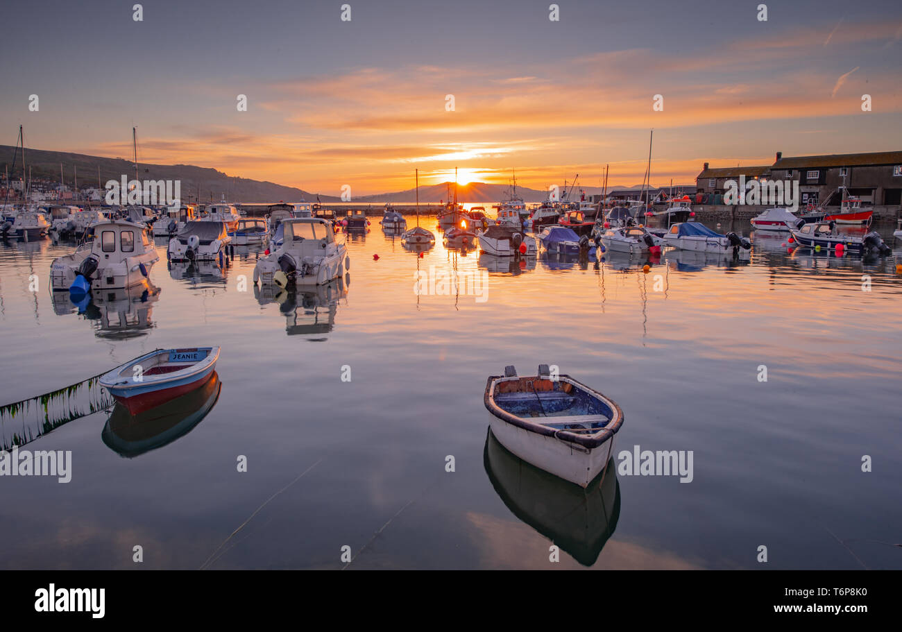 Lyme Regis, Dorset, UK. 2nd May 2019. UK Weather: Fishing boats and vibrant sunrise colours are reflected in the calm water at the Cobb at Lyme Regis on a beautiful spring morning. Credit: Celia McMahon/Alamy Live News. Stock Photo