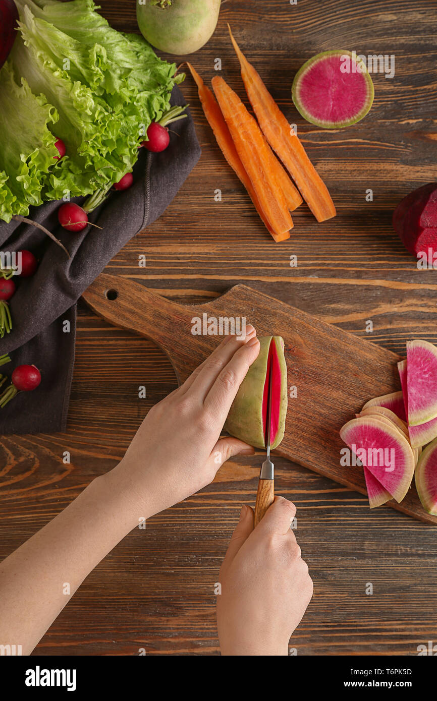 Woman cutting ripe radish on wooden board, top view Stock Photo - Alamy