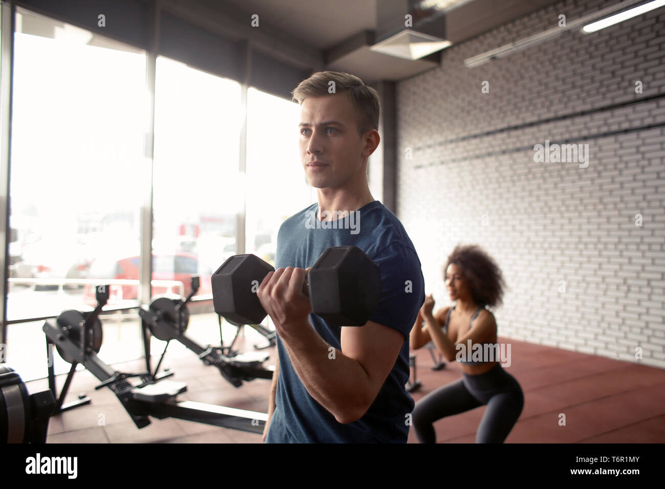 Athletic man doing exercise with dumbbell in modern gym Stock Photo