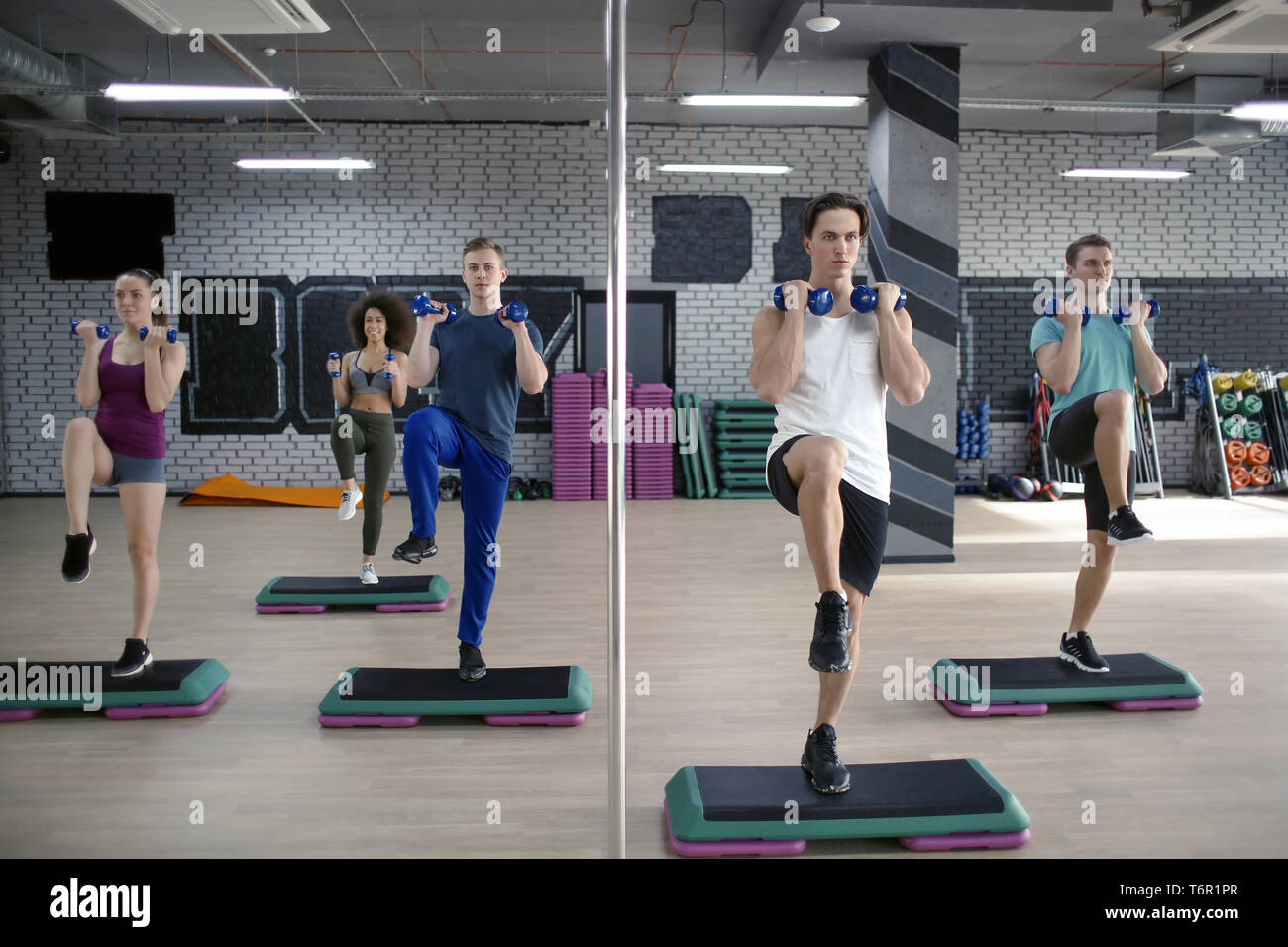 Group of young people working out with dumbbells and steppers in gym Stock Photo