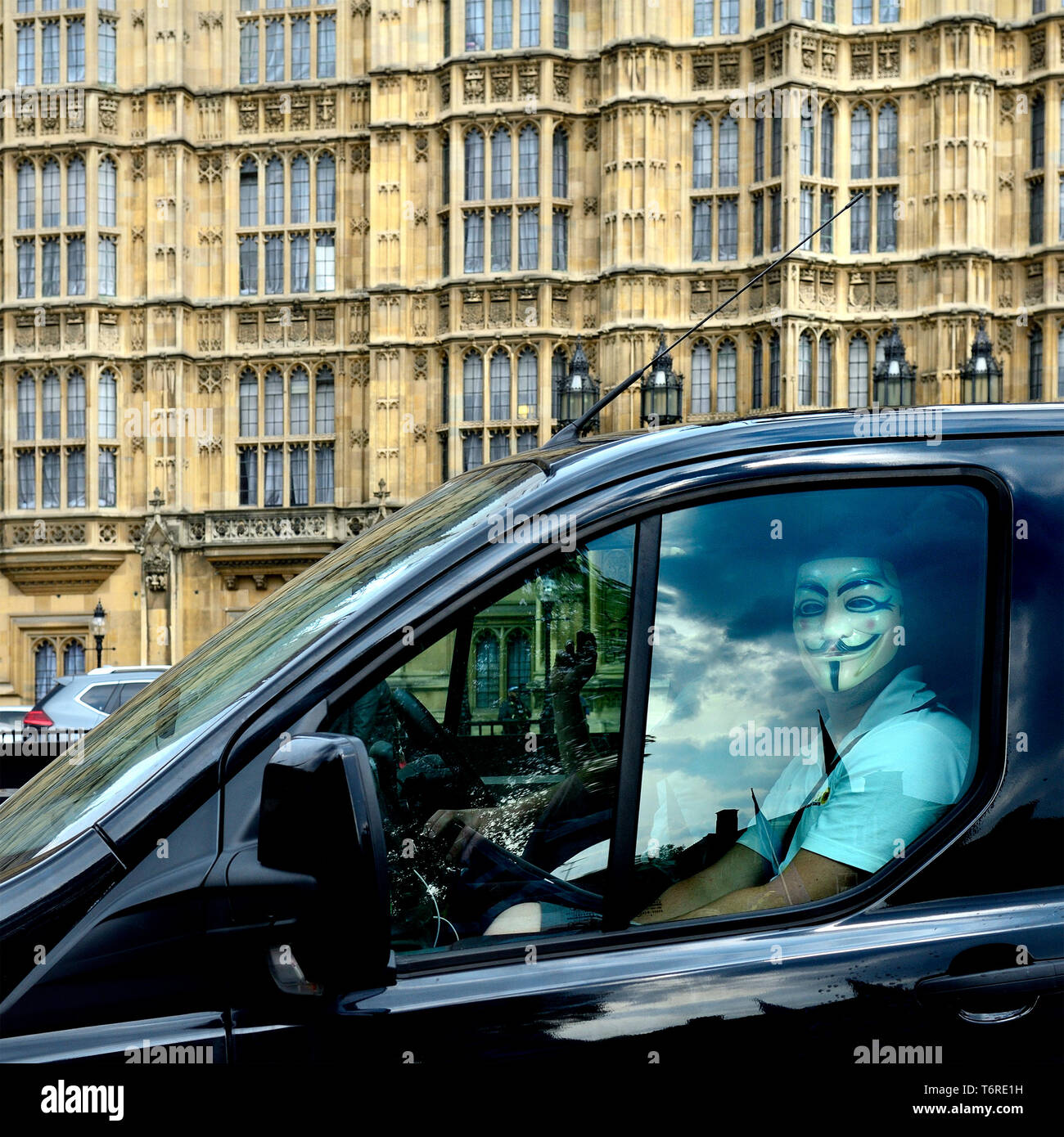 London, England, UK. Man wearing a V for Vendetta mask in the passenger seat of a van, passing the Houses of Parliament Stock Photo