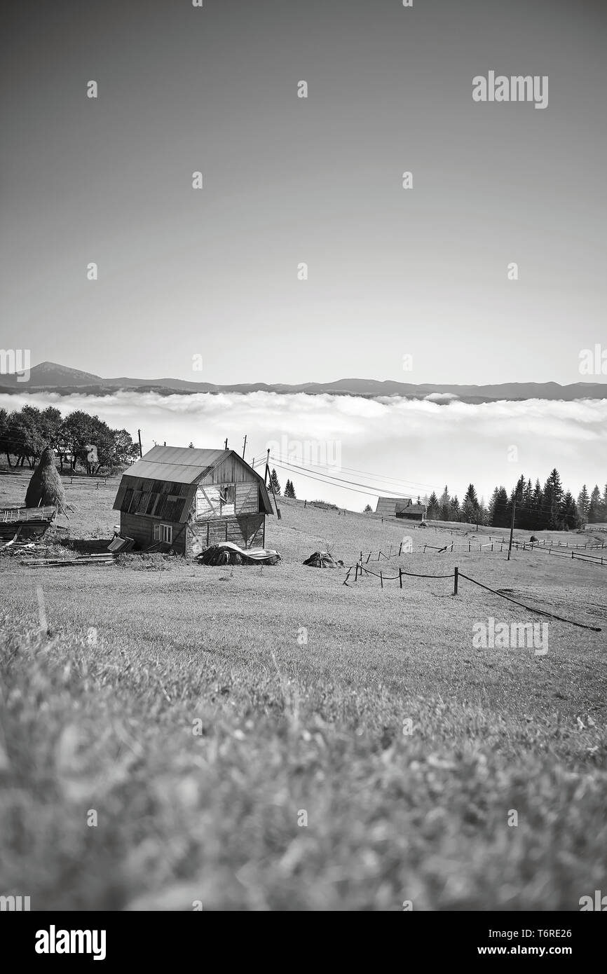 Fantastic black and white landscape foggy morning in Carpathian village, a small wooden hut on meadow, Ukraine Stock Photo
