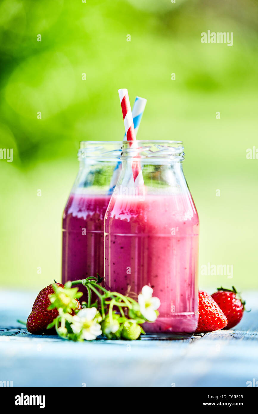 Bright, vibrant, summer strawberry smoothies in glass jars on an outdoor summer picnic table setting. Stock Photo