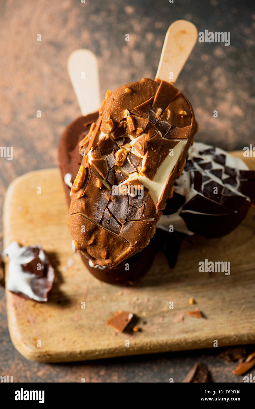 closeup of some chocolate ice cream bars on a chopping board, placed on a rustic wooden table sprinkled with cocoa powder and pieces of chocolate Stock Photo