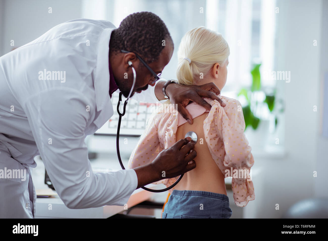 Dark-skinned pediatrician using stethoscope while examining girl Stock Photo