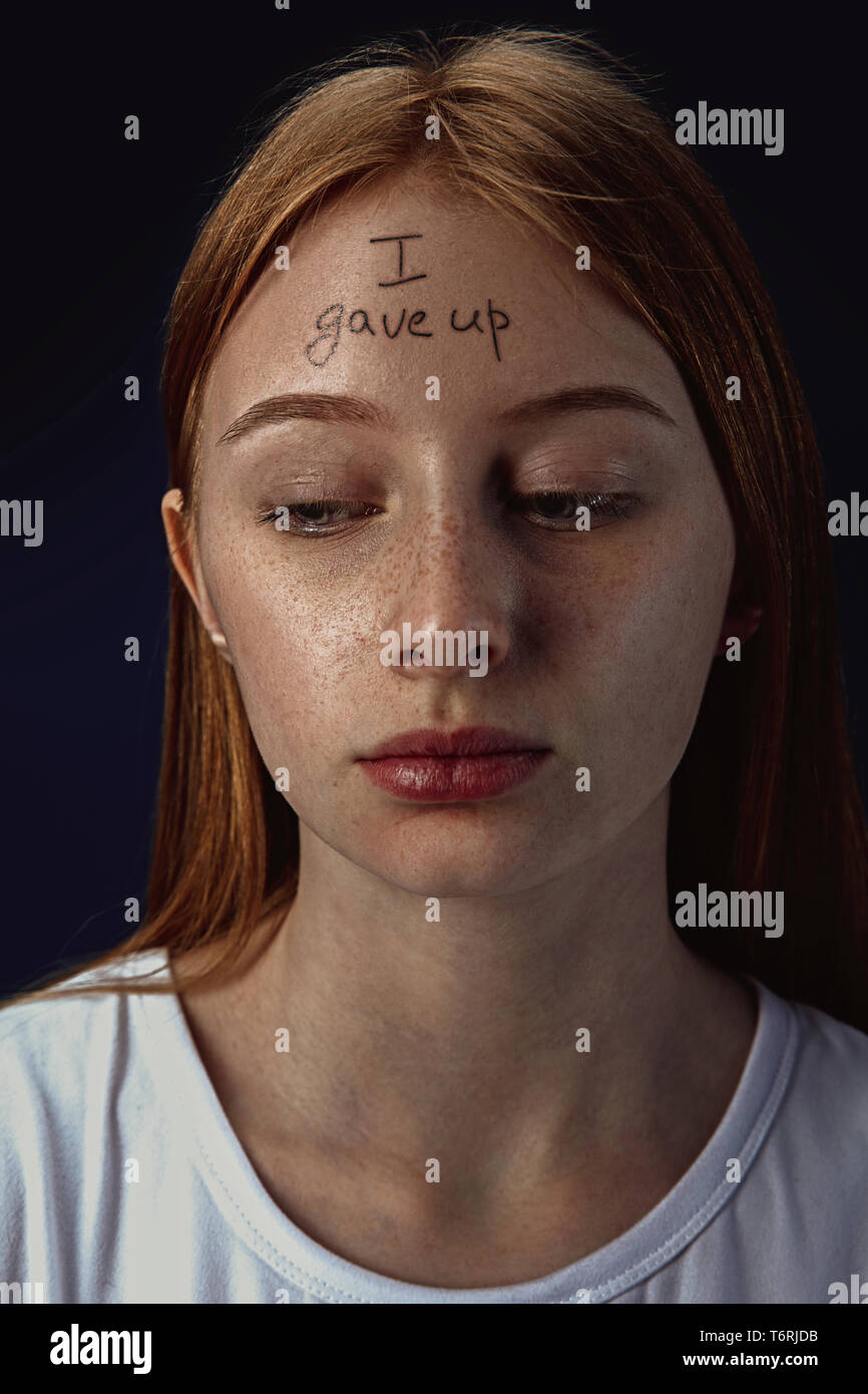 Portrait of young woman with mental health problems. The image of a tattoo on the forehead with the words I gave up. Concept of hidding the true feelings, psycological trouble, treatment. Stock Photo