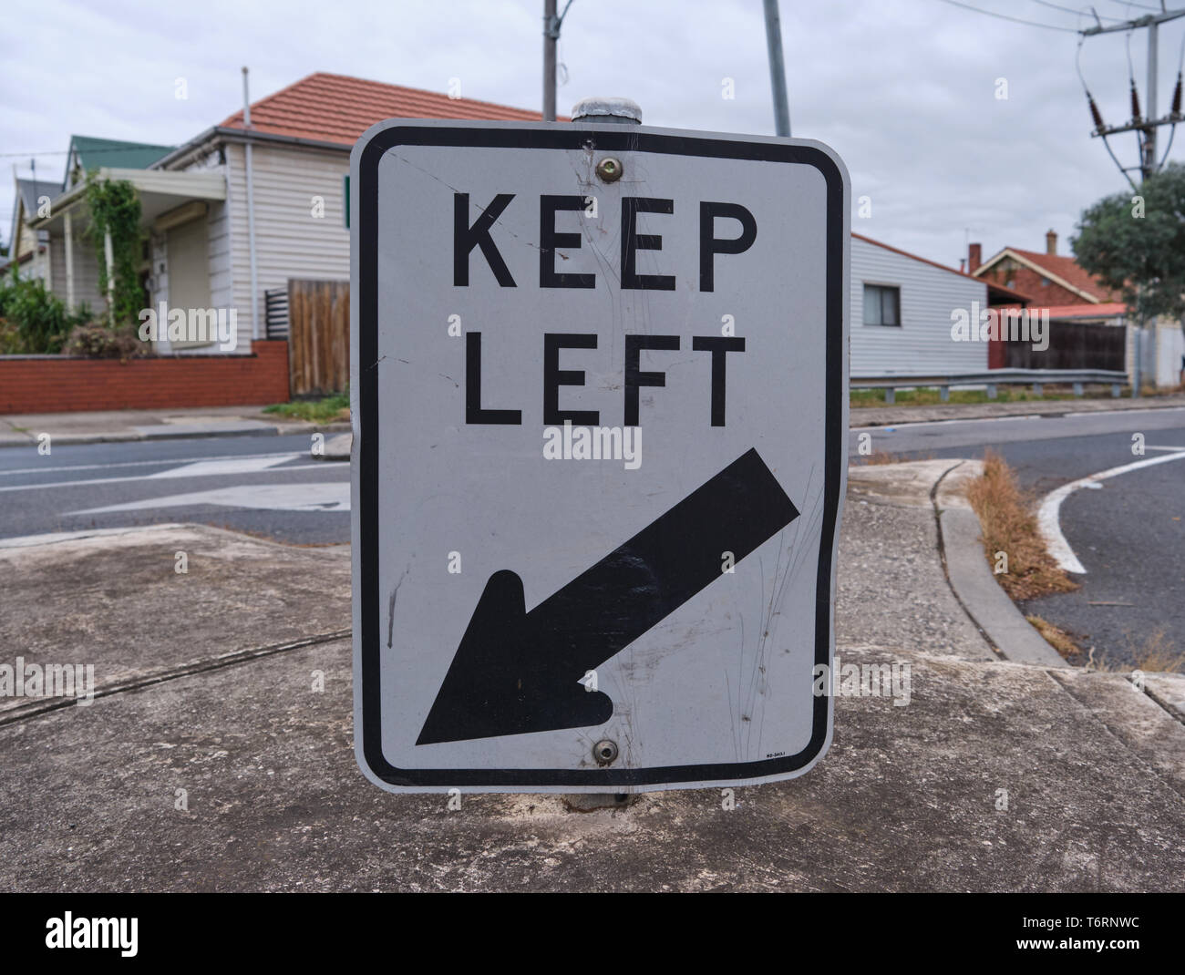 Road sign Keep Left in middle of cement median with cloudy sky and house in background in Melbourne, Australia Stock Photo