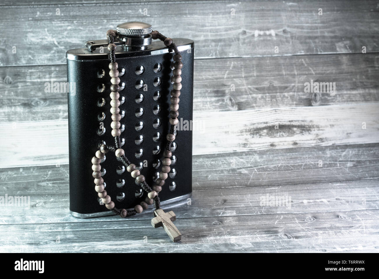 Wooden rosary wrapped around a standing, black leather hip flas with some stainless steel elements Stock Photo